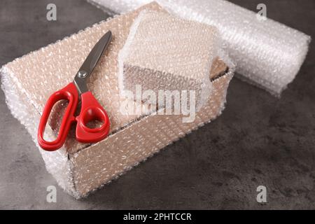 Cardboard boxes, bubble wrap and scissors on dark grey table Stock Photo