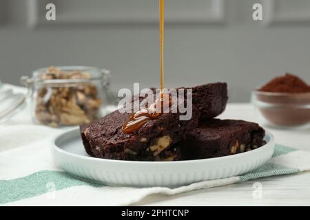 Pouring caramel sauce onto delicious chocolate brownies with nuts on white table Stock Photo