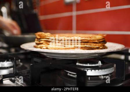 Plate of freshly made crepes on stove in kitchen, closeup Stock Photo