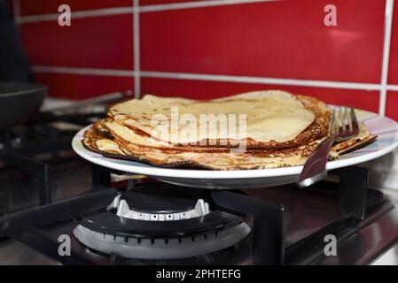 Plate of freshly made crepes with fork on stove in kitchen, closeup Stock Photo