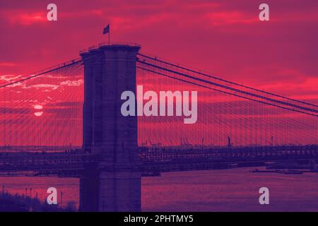 The setting sun paints a colorful sky behind the Brooklyn Bridge in New York City with red and blue color effect Stock Photo