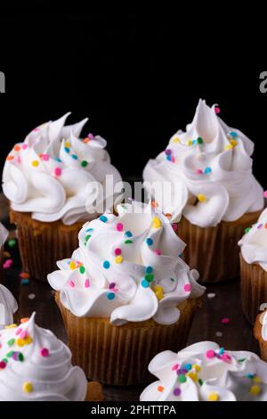 Fluffy vanilla cupcakes, with meringue and dragees on a black background, original recipe Stock Photo