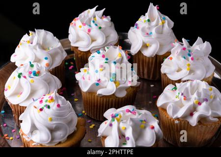 Fluffy vanilla cupcakes, with meringue and dragees on a black background, original recipe Stock Photo
