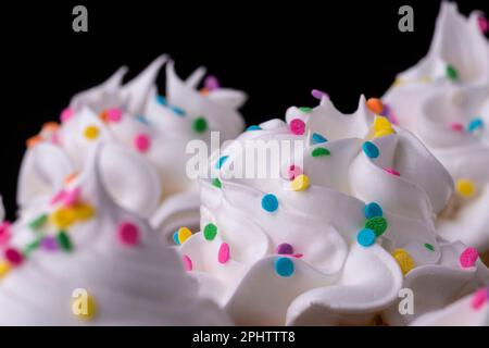 Fluffy vanilla cupcakes, with meringue and dragees on a black background, original recipe Stock Photo