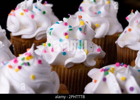 Fluffy vanilla cupcakes, with meringue and dragees on a black background, original recipe Stock Photo