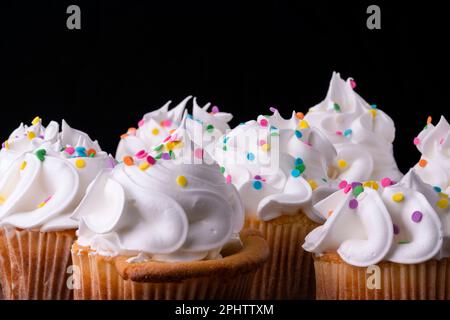 Fluffy vanilla cupcakes, with meringue and dragees on a black background, original recipe Stock Photo