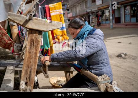 Muktinath, Nepal - November 20, 2021: A woman weaving scarves on an old loom in the streets of Muktinath. Stock Photo