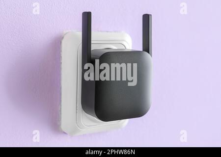 Black WiFi repeater in electric socket on lilac wall Stock Photo
