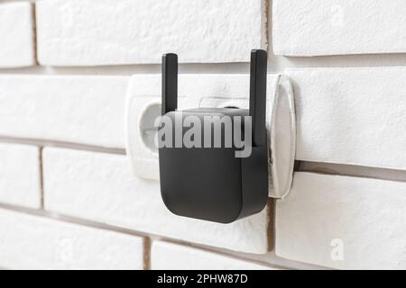 Black WiFi repeater in electric socket on white brick wall Stock Photo
