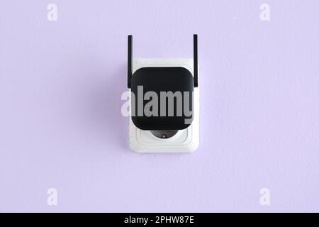 Black WiFi repeater in electric socket on lilac wall Stock Photo