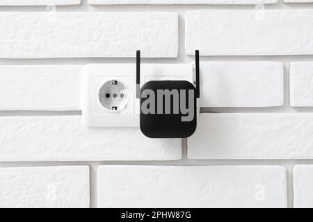Black WiFi repeater in electric socket on white brick wall Stock Photo