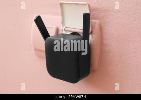 Black WiFi repeater in electric socket on pink wall Stock Photo