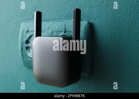 Black WiFi repeater in electric socket on green wall Stock Photo