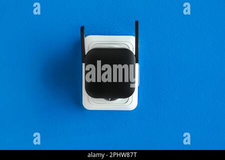 Black WiFi repeater in electric socket on blue wall Stock Photo