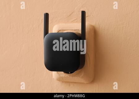 Black WiFi repeater in electric socket on beige wall Stock Photo