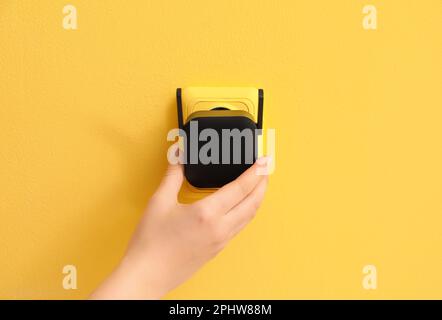 Woman plugging black WiFi repeater in electric socket on yellow wall Stock Photo