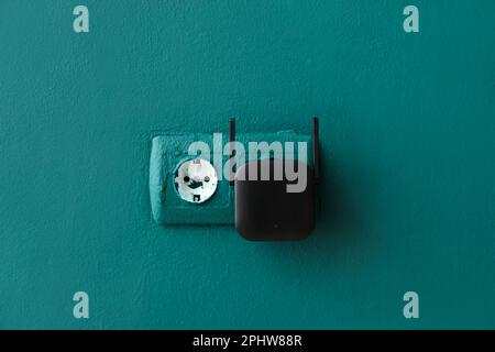 Black WiFi repeater in electric socket on green wall Stock Photo