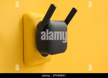 Black WiFi repeater in electric socket on yellow wall Stock Photo