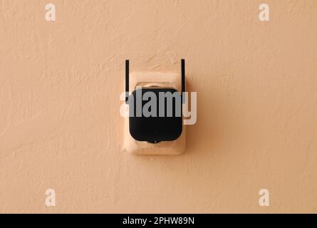 Black WiFi repeater in electric socket on beige wall Stock Photo
