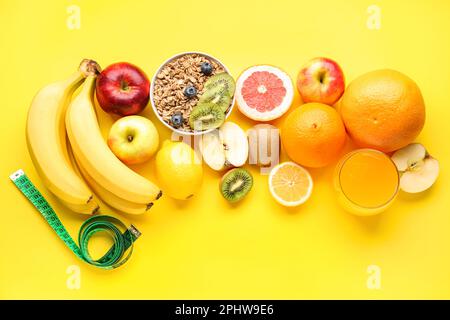 Fruits, oatmeal flakes and green measuring tape on yellow background. Diet concept Stock Photo