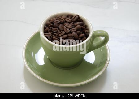 Green medium size coffee cup filled with whole roasted coffee beans Stock Photo