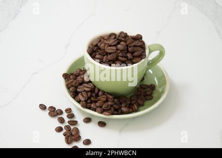 Green medium size coffee cup filled with whole roasted coffee beans Stock Photo