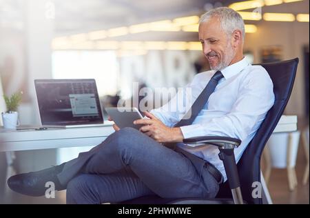 Studying business trends online. a mature businessman using a digital tablet in an office. Stock Photo
