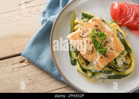 Roasted wild salmon fillet with parsley garnish on creamy zucchini vegetables and fresh tomato on a light plate, healthy meal for a low carb diet, hig Stock Photo