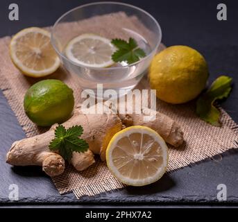 Composition of ginger and lemon, with green leaves and a container with lemon slice in water Stock Photo