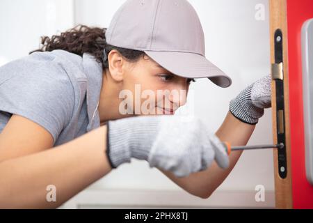 happy female builder using a screwdriver on a door Stock Photo