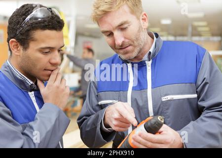 foreman overseeing apprentice using drill on wall Stock Photo