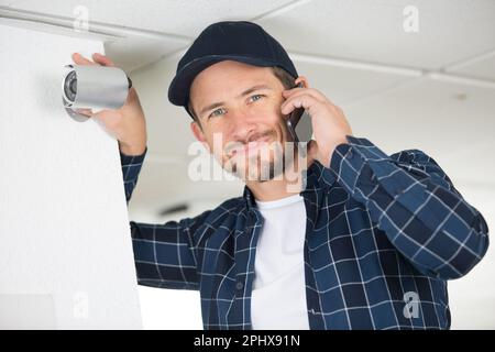 cotractor taking voice call on smartphone while checking cctv camera Stock Photo