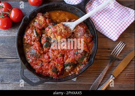 Zucchini roulades stuffed with ground beef and cooked in a delicious tomato sauce. Italian involtini. Served in a cast iron pan on wooden table Stock Photo