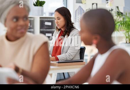 Coworking, serious and woman sitting in an office, working and focused on a corporate job. Team, business and a group of diverse employees in the Stock Photo