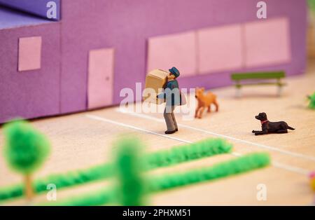 From above side view of plastic toy courier carrying carton box to client in house with dogs in front Stock Photo