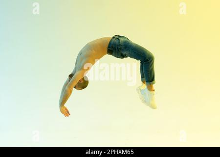 Fit male athlete performing a flick flack jump or back handspring in a full length side view over a colorful studio background Stock Photo