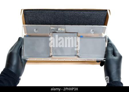Hands in black gloves hold a replacement battery for a laptop packed in a plastic package isolated on white. Stock Photo