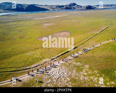 Aerial drone view of crowd people running competition down dusty country road near river and hills at sunset. Trail running at the steppe near Ili riv Stock Photo