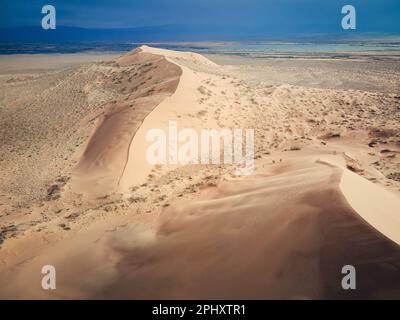 Aerial drone view shot of Singing Sand desert dunes barkhan landscape and ili river in famous place Altyn Emel National Park near Almaty, Kazakhstan Stock Photo