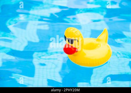 Inflatable Swimming duck Ring floating in the pool. Yellow plastic duck with sunglasses Stock Photo