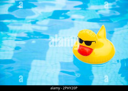 Inflatable Swimming duck Ring floating in the pool. Yellow plastic duck with sunglasses Stock Photo