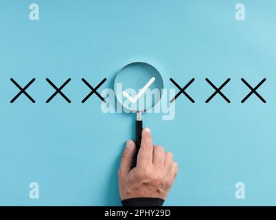 Focusing on the right choice concept. Hand holds magnifying glass focusing on the checkmark or tick right symbol next to wrong cross icons. Stock Photo