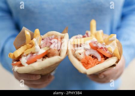 Woman holding two gyros pita sandwiches in hands. Female person holds traditional Greek fast food with grilled meat, fries and tzatziki sauce wrapper Stock Photo