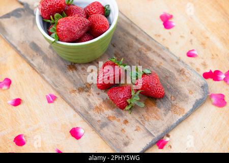 Wet wooden board with bowl with strarwberries and three strawberries lying on table. Stock Photo