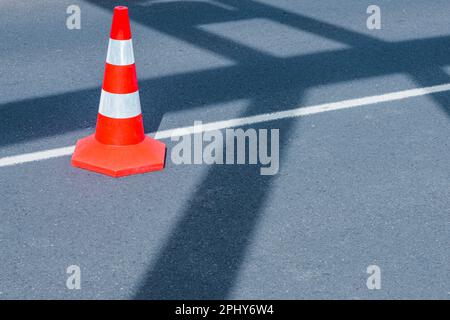 A bright red traffic cone stands alone on an asphalt city street, warning drivers of potential hazards ahead with its security symbol. Stock Photo