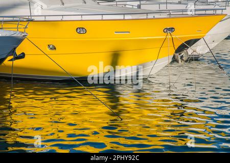 The hull of a bright yellow luxury yacht with its bright colour reflected in the water on the Puerto Banus marina, Marbella; Spain Stock Photo