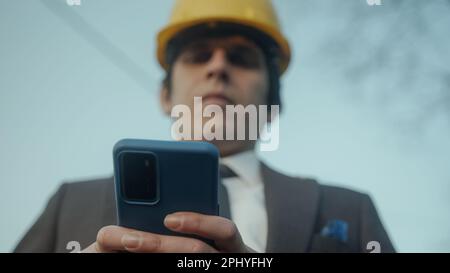 Construction Engineer or Contractor in a Suit Messaging or Using an App on His Smartphone Outdoors Stock Photo