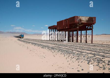 A vintage, corroded metal structure situated in a desert landscape with railroad tracks stretching out in either direction Stock Photo