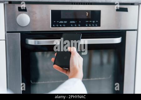 Young woman is indoors in smart house room controlling the oven Stock Photo