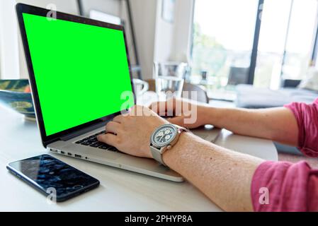Young professional man using a laptop with a green screen - wearing a fashion watch. Work from home - London, United Kingdom, 1st of June 2019 Stock Photo